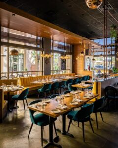 Wide angle interior view of The Yellow Chilli USA restaurant dining hall with timber tables and teal chairs by Urban Box Studio