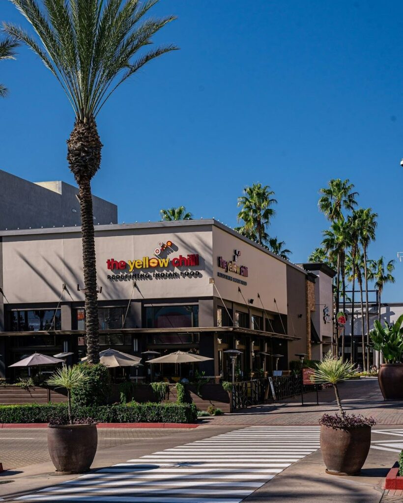 Exterior storefront view of The Yellow Chilli USA restaurant showing modern facade signage and patio seating framed by palm trees by Urban Box Studio