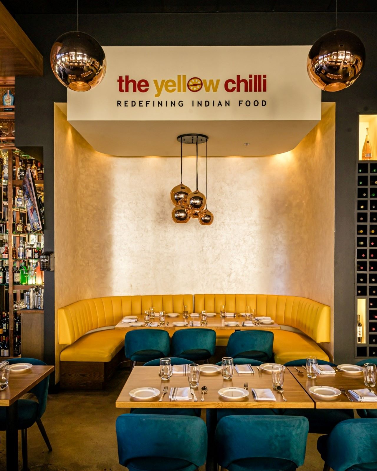 Signature semi-circular yellow banquette booth with copper cluster lights and brand wall logo at The Yellow Chilli USA by Urban Box Studio