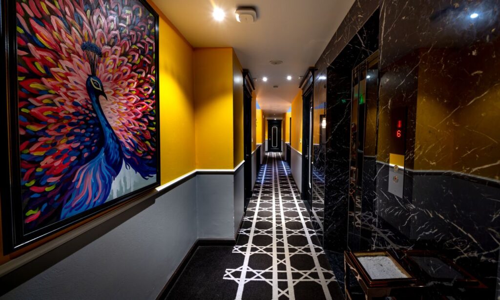 A colorful hotel corridor featuring a vibrant peacock painting on the wall.