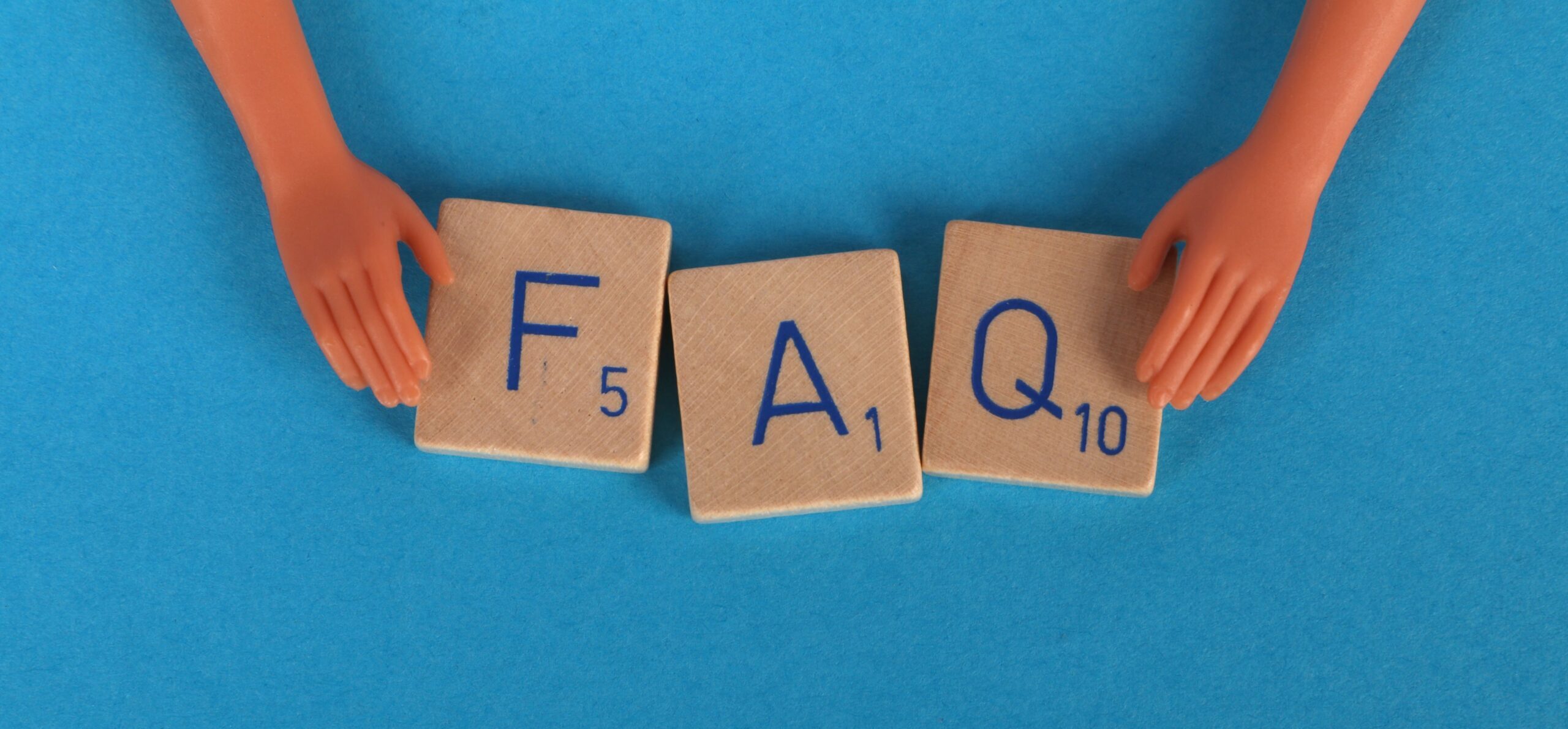 Flat lay of scrabble tiles spelling 'FAQ' with toy hands on a blue background, creating a conceptual image.